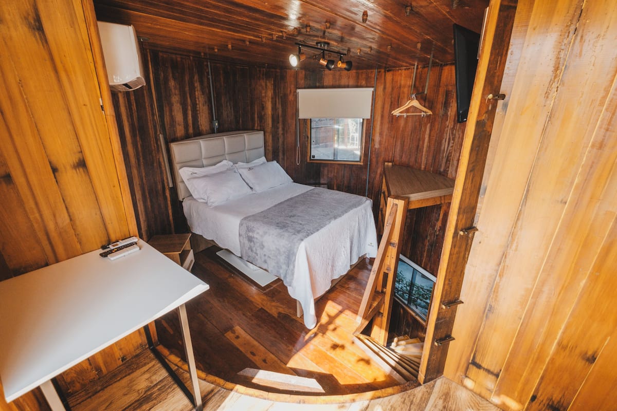 A wooden cabin bedroom with a bed, a table, and a window.