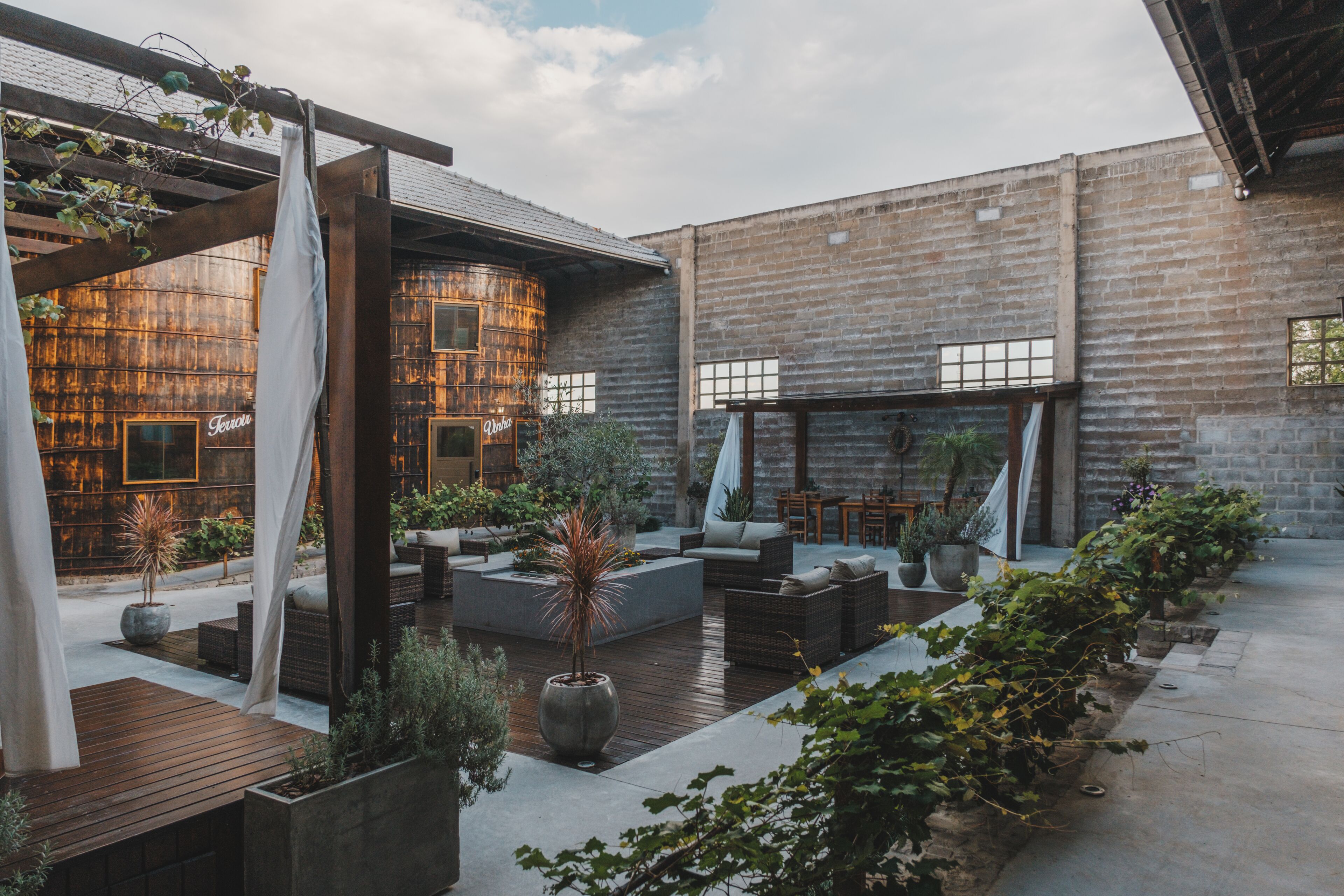 An outdoor patio area with seating, planters, and a brick building in the background.