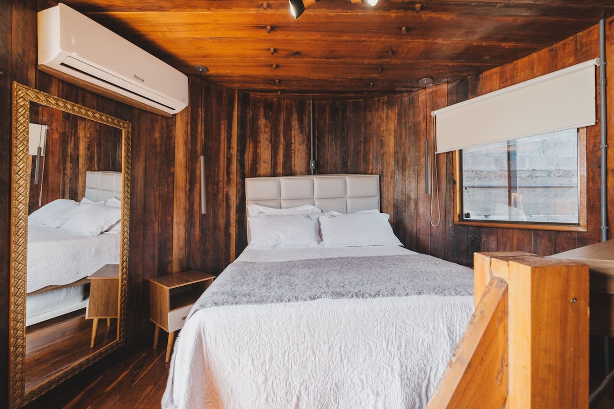 A wooden room with a bed, a large mirror, and an air conditioning unit.