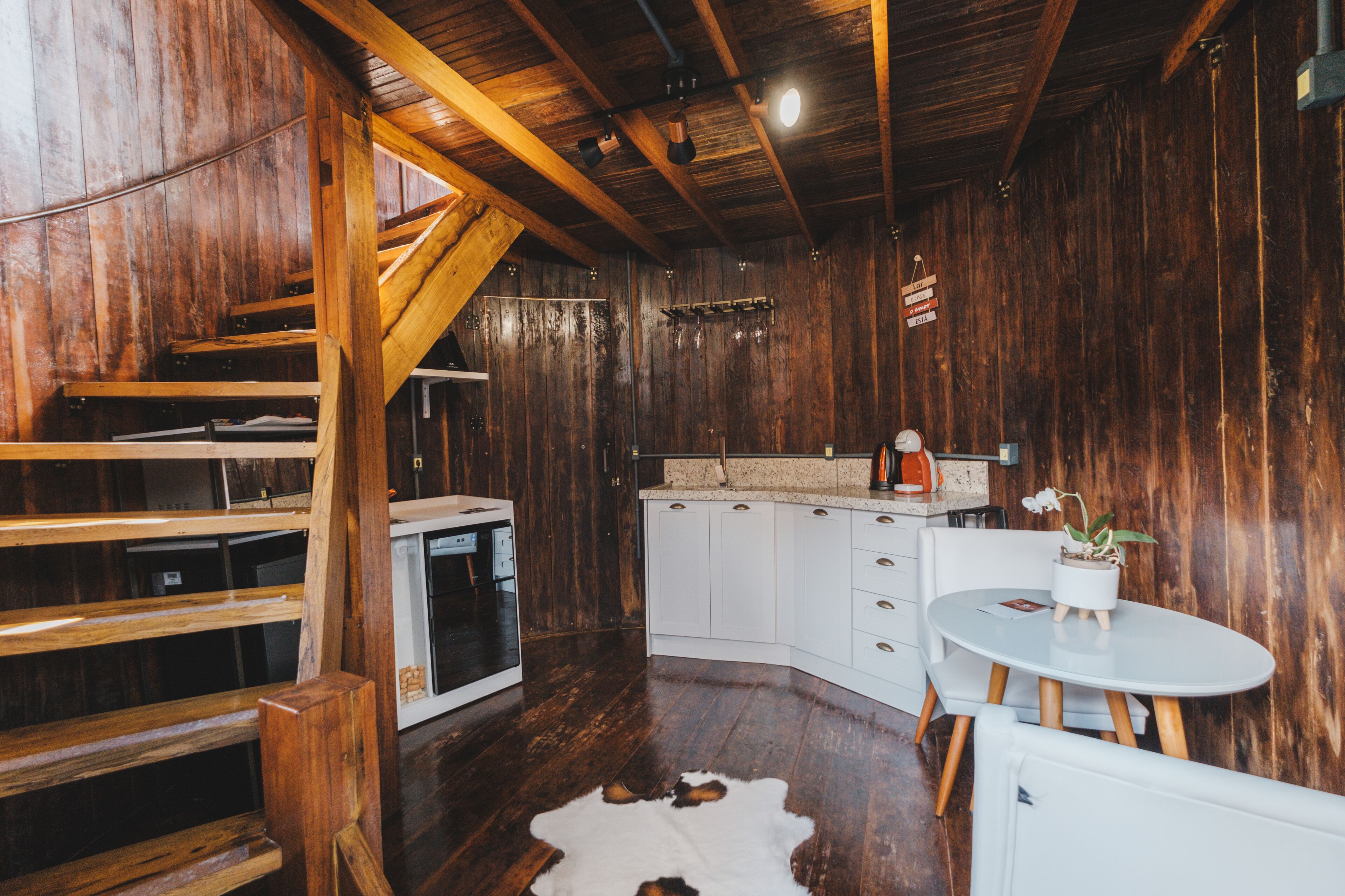 A rustic interior with wooden walls, a white kitchen, and a cowhide rug.