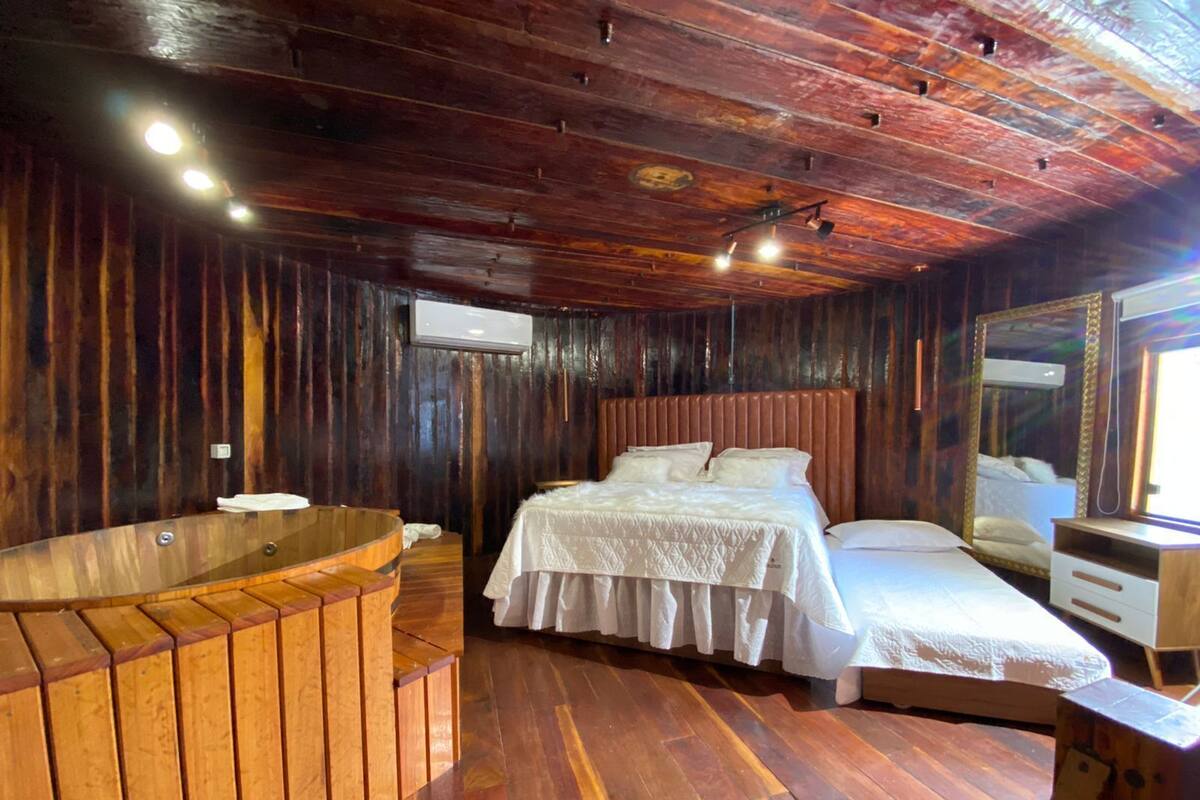 A wooden room with a bed, a small table, a mirror, and a wooden bathtub.