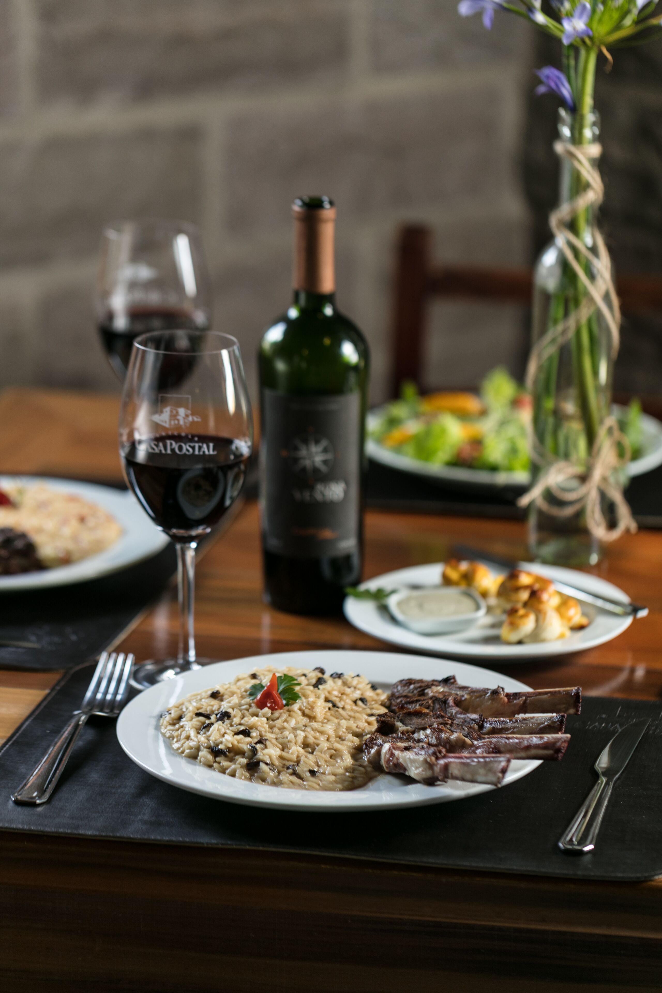 A dining table with plates of food, a wine glass, and a bottle of wine.