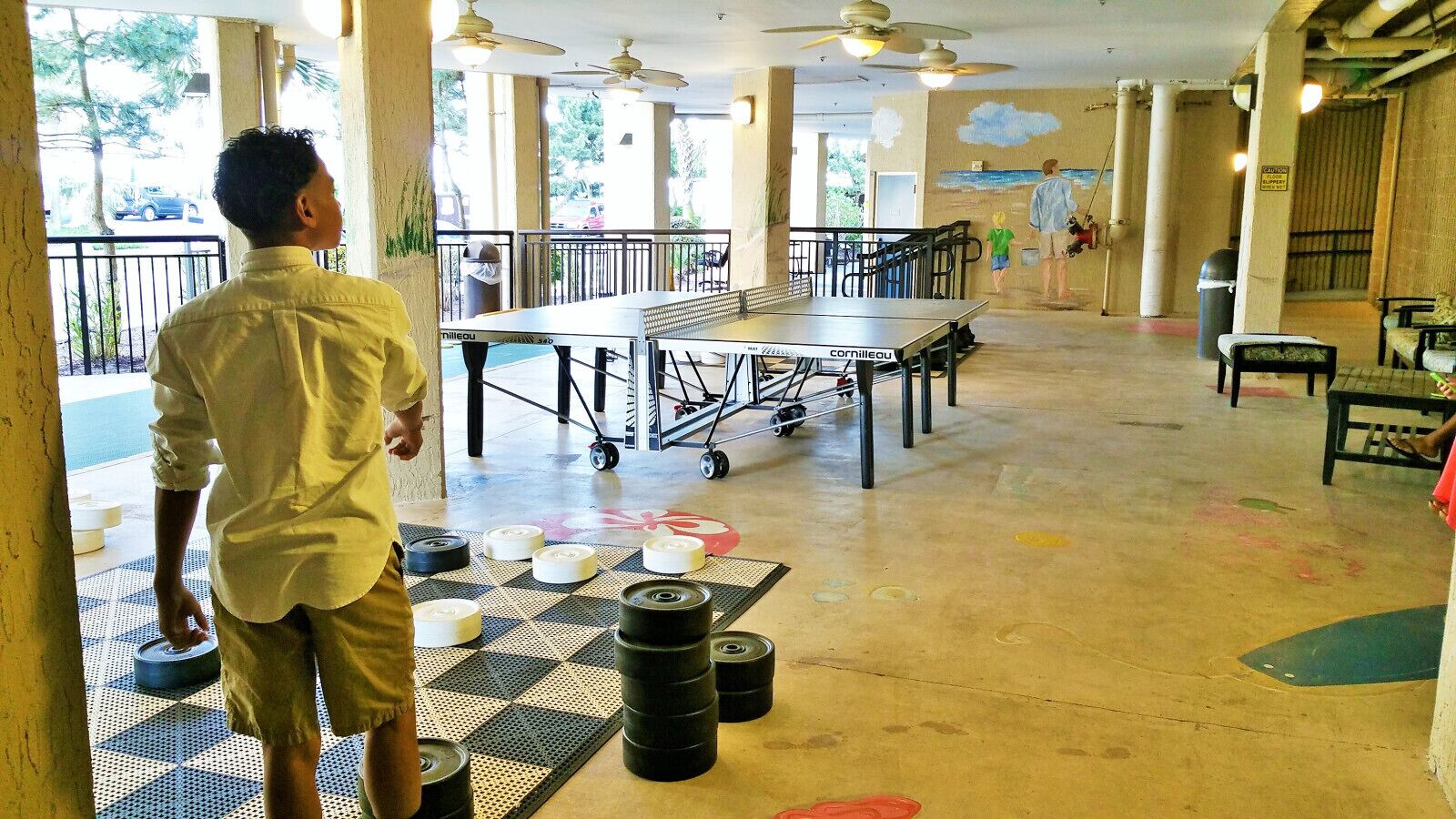Un grand espace intérieur comprenant une table de ping-pong, du matériel d’exercice et une fresque murale.