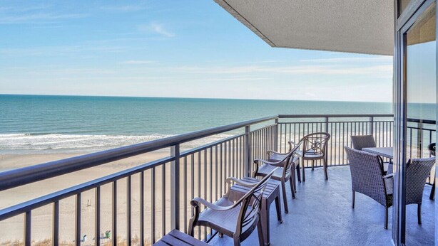 A balcony with a view of the ocean, furnished with wicker chairs and a table.