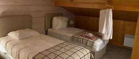 Una habitació petita i acollidora amb dos llits, parets de fusta i sostre inclinat.