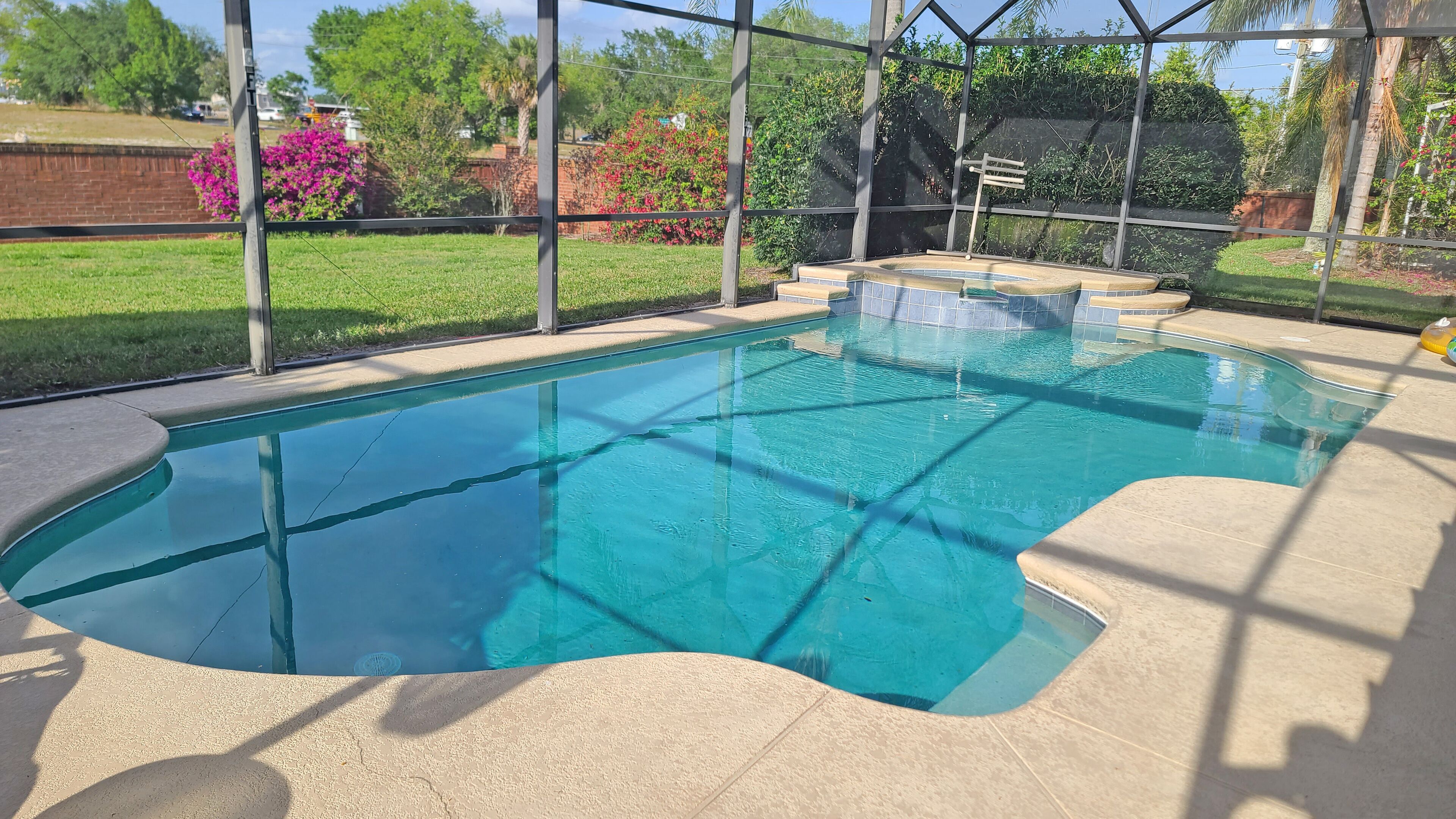Una piscina con agua cristalina, rodeada por un área techada con vistas a un jardín y árboles.