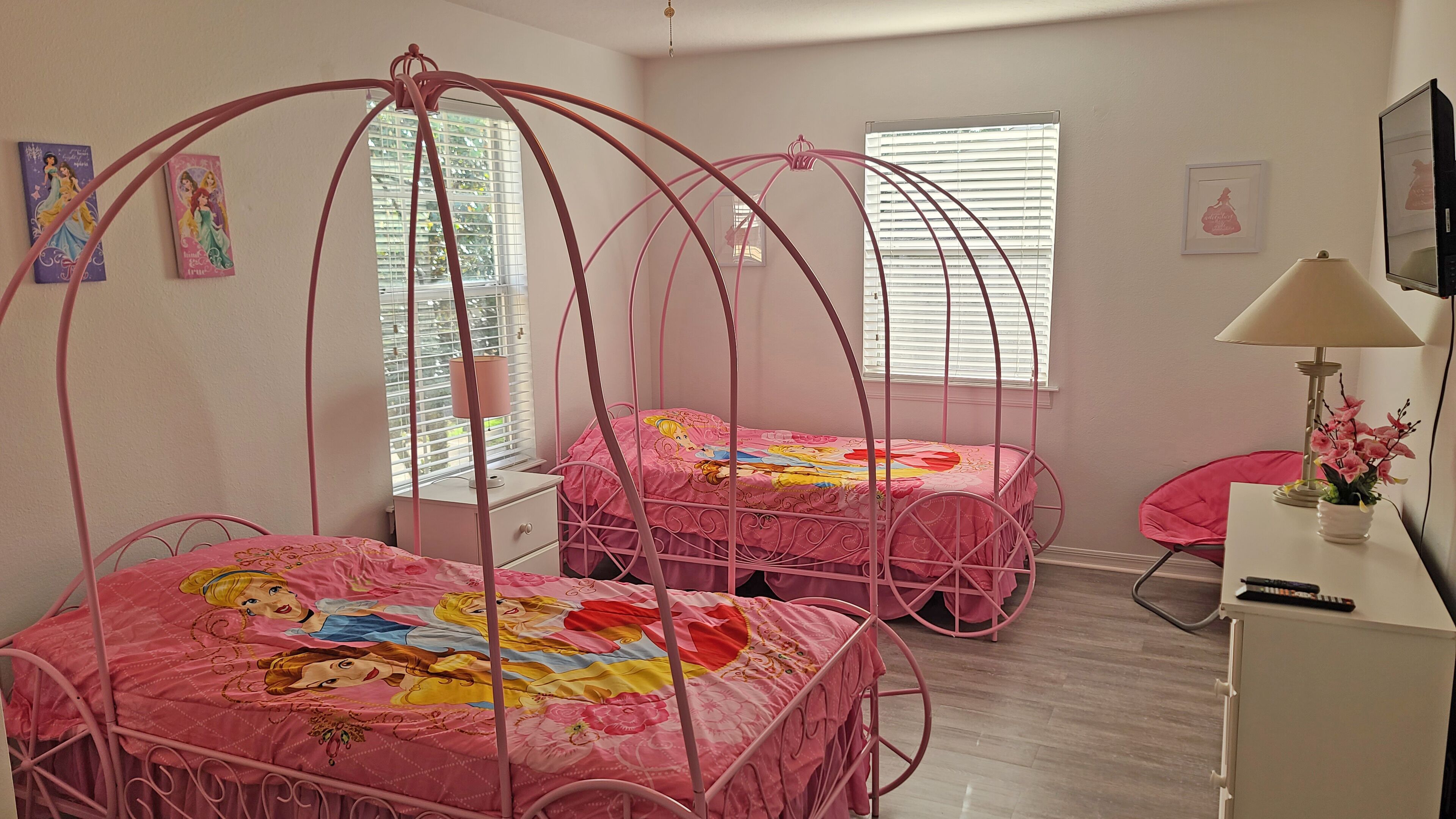 A bedroom with two pink beds, a white dresser, a desk with a lamp, and a TV.