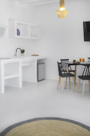 A modern kitchen with white cabinetry, a built-in refrigerator, and a dining area with black chairs and a small table.