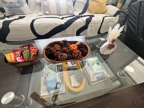 A glass-top table with a bowl of pinecones, a small plant, and a welcome bag.