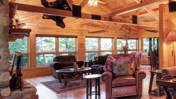 A spacious cabin with a high ceiling, wooden beams, and large windows offering views of the surrounding forest. - On the Eagle River Chain O’ Lakes, Lake Front, 3200 sq. ft., 2.5 baths (Eagle River)