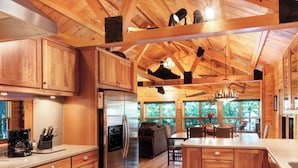 A wooden cabin interior with a kitchen, dining area, and a large window offering a view of the outdoors. - On the Eagle River Chain O’ Lakes, Lake Front, 3200 sq. ft., 2.5 baths (Eagle River)