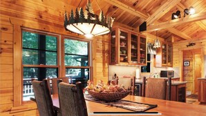 A wooden cabin interior with a dining area, kitchen, and large windows. - On the Eagle River Chain O’ Lakes, Lake Front, 3200 sq. ft., 2.5 baths (Eagle River)