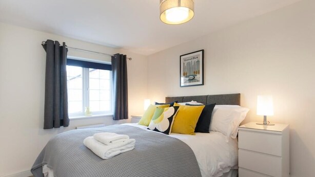 A neatly made bed with a grey and white bedspread, a set of folded towels, and a bedside lamp on a white nightstand. - The Terrace (Derby)