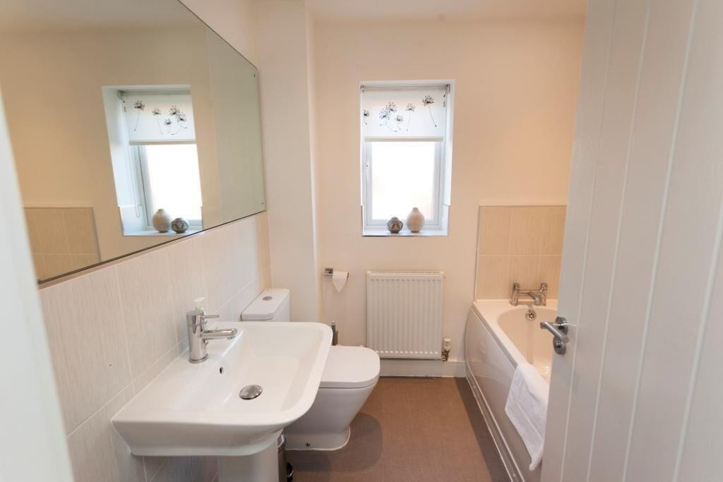 A compact bathroom with a white sink, toilet, and bathtub. There are two windows with decorative curtains.