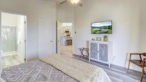 Un dormitorio con una cama, un ventilador de techo, un armario blanco con puertas decorativas y un televisor en la pared.