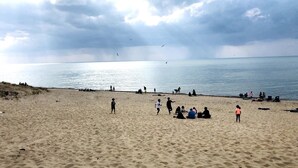 Une vaste plage de sable où l’on voit des gens dispersés, certains assis, d’autres debout.