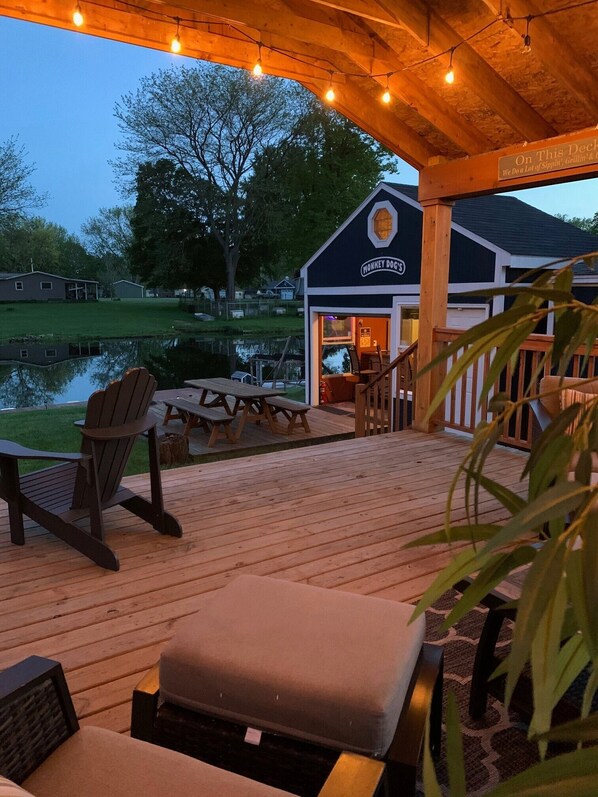 A wooden deck with outdoor seating, a sign for 'Monkey Docs', and a view of a lake.