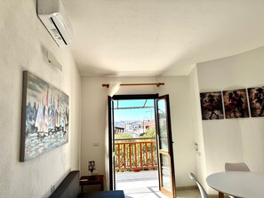 A room with a balcony, a painting of sailboats, a table, and a chair.