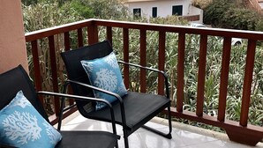 Varanda com duas cadeiras pretas e almofadas azuis, com vista para uma área residencial com edifícios e vegetação.