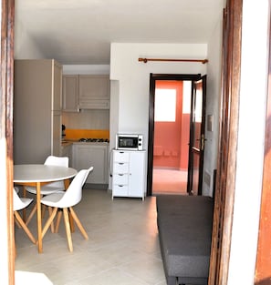 A compact kitchen with a microwave, a dining table with chairs, and a bench.