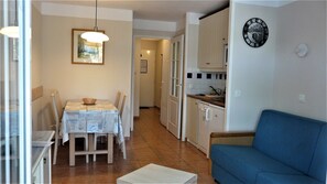 A compact living space with a dining area, kitchenette, and a blue sofa. - Among the pines, between nature and the ocean (Lacanau)