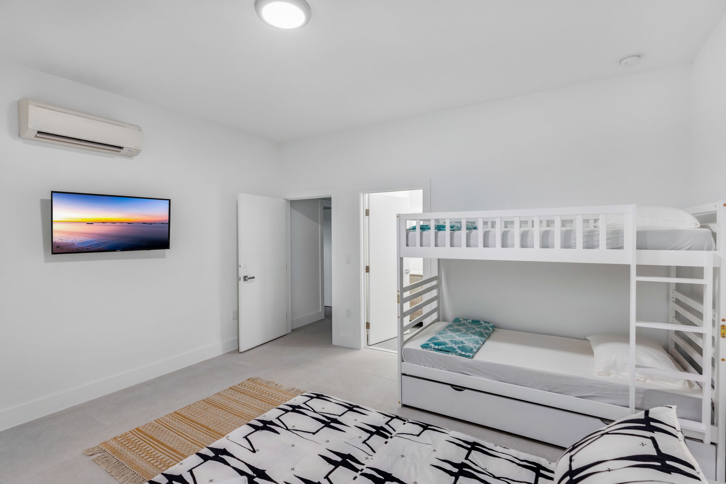 Una camera da letto con un letto a castello, una TV a schermo piatto, una porta che dà su un'altra stanza e un tappeto decorato.