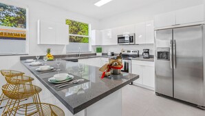 Cozinha moderna com armários brancos, eletrodomésticos de aço inoxidável, bancada de granito e uma ilha central com assentos.