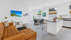 Uma cozinha moderna com armários brancos, uma área de jantar com mesa redonda e uma sala de estar com sofá marrom.