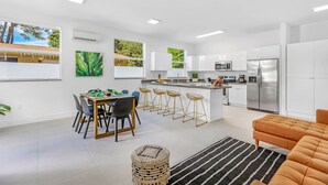 Cozinha moderna com armários brancos, geladeira de aço inoxidável e um espaço bar com banquetas.