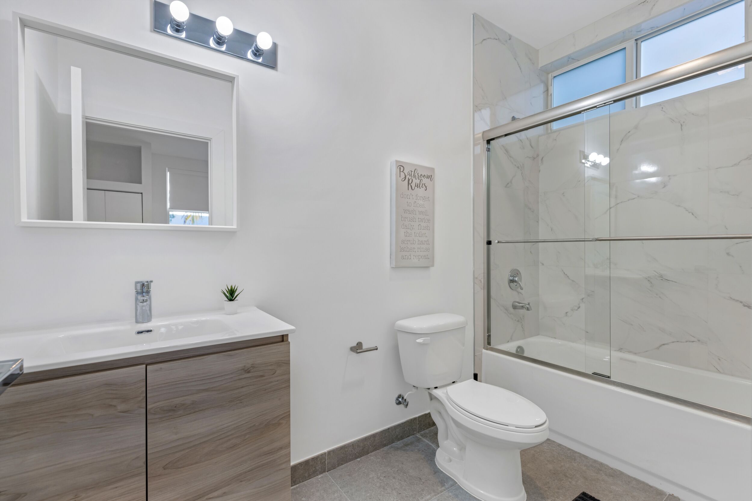 Une salle de bain avec un meuble-lavabo blanc, des toilettes, une douche avec une porte en verre et un miroir surmonté de luminaires.