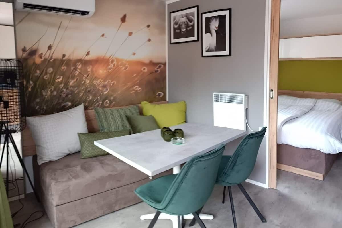 Habitación pequeña con sofá, una mesita, dos sillas, una cama litera y aire acondicionado de pared.