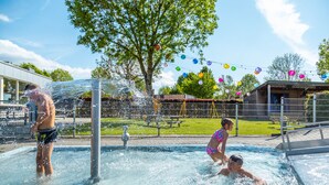 Una piscina con chorros de agua, rodeada de una valla y árboles.