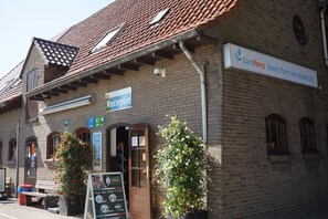 Un bâtiment en briques avec une enseigne indiquant « EuroParcs Resort Poort van Maasbracht », un espace d’accueil et un banc à l’extérieur.