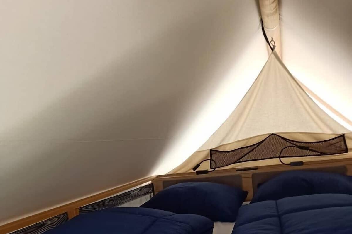 Una habitación tipo tienda de campaña con cama, dosel y cabecera de madera.