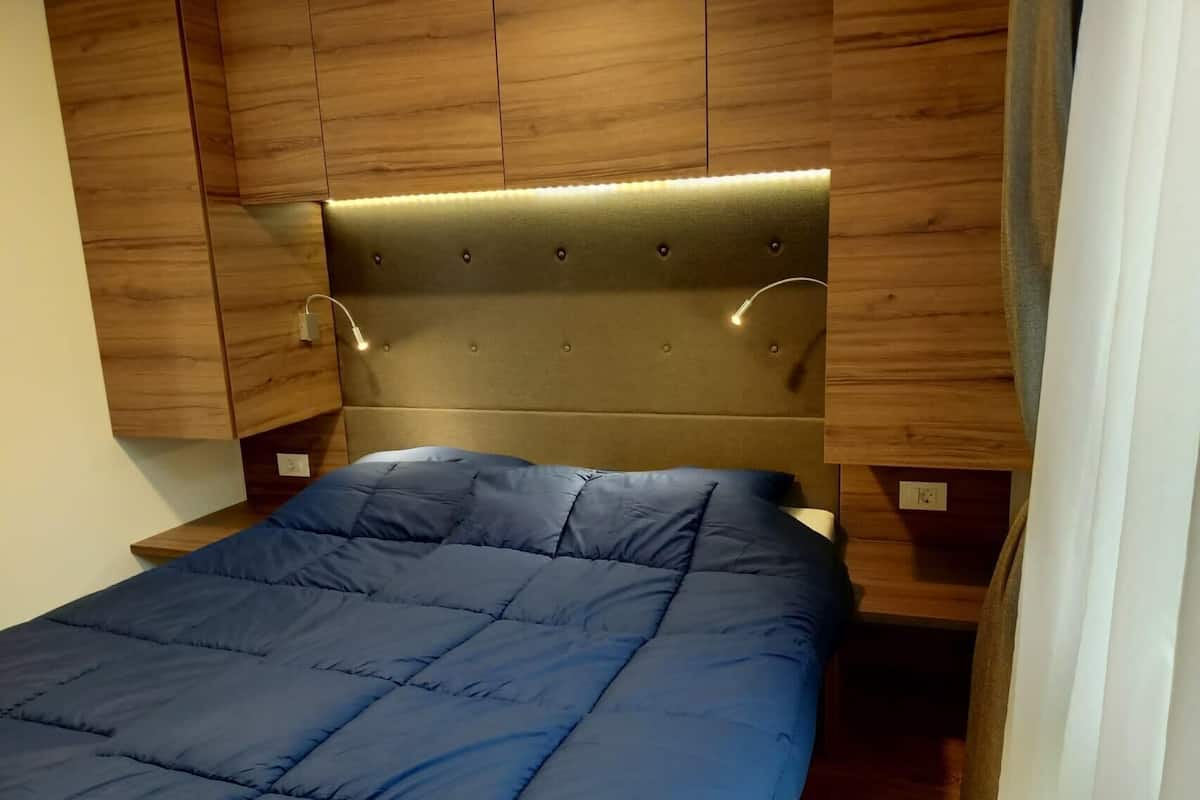 Una cama con colcha azul, cabecero de madera y lámparas de noche.