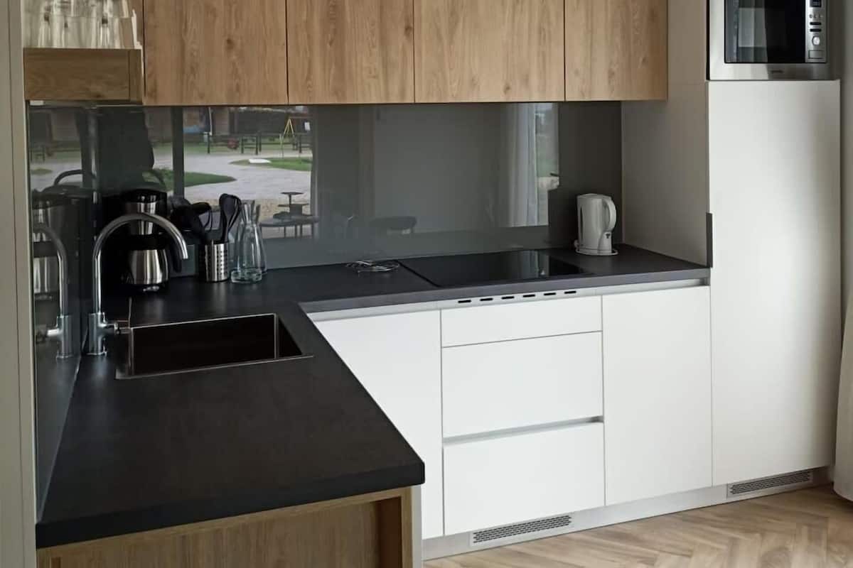 Una cocina moderna con armarios de madera, encimera negra, electrodomésticos de acero inoxidable y vistas al exterior.
