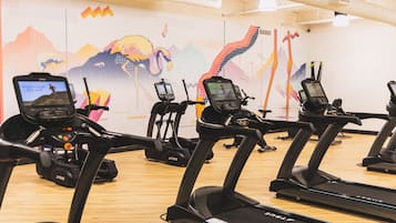 A gym with multiple treadmills and exercise bikes, equipped with digital screens.