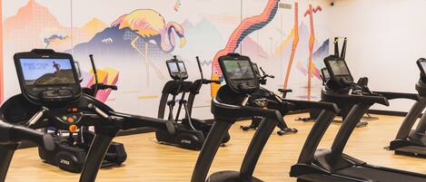 A gym with multiple treadmills and exercise bikes, equipped with digital screens.