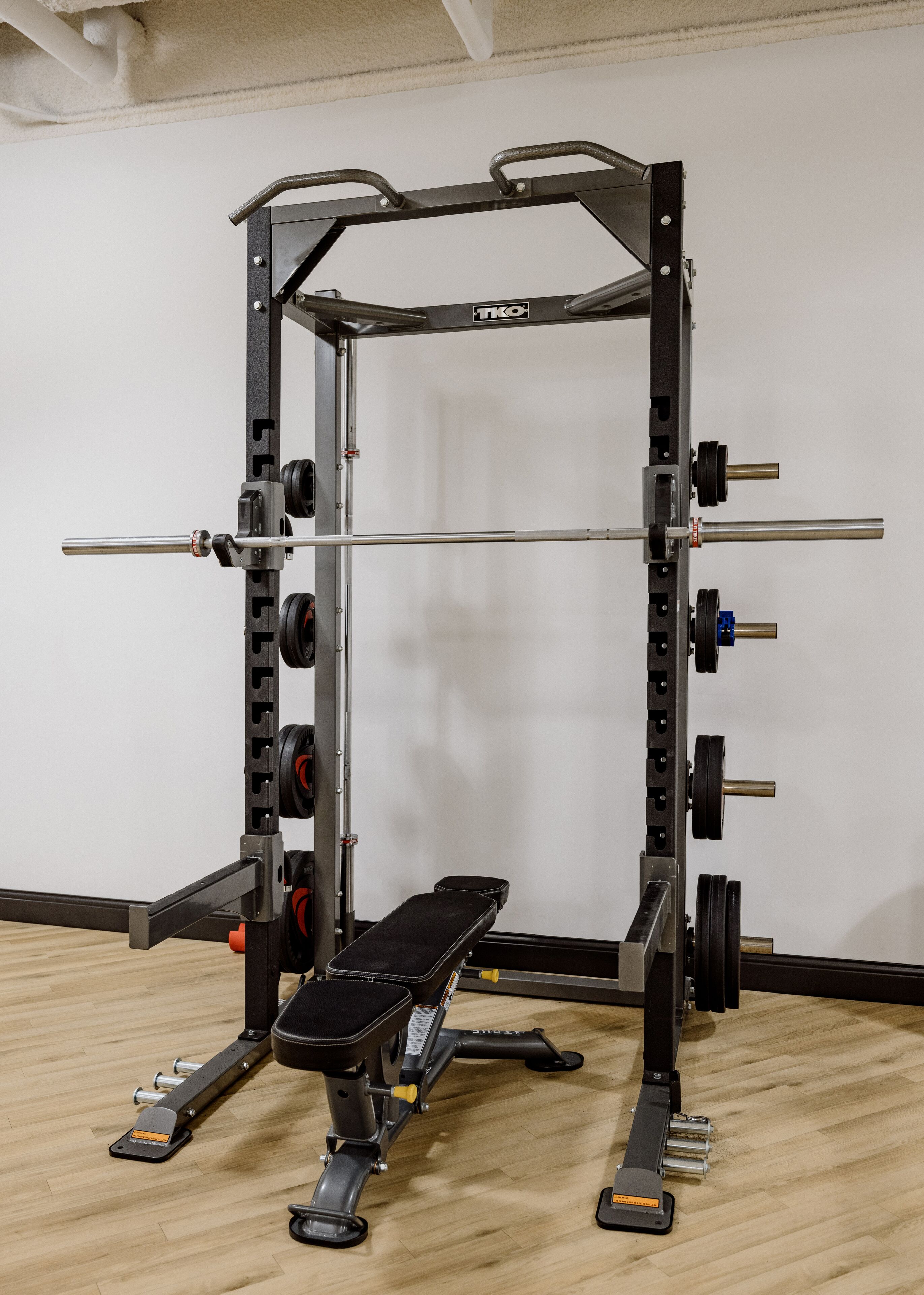 Un espace d’entraînement dédié à la musculation, équipé d’un banc, d’un support à squats et de différents disques de poids.