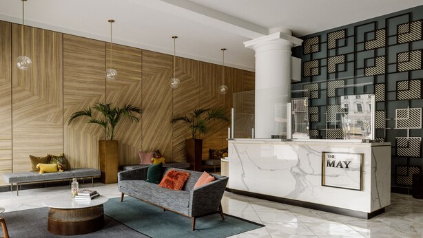 A modern lobby with a marble reception desk, a grey sofa with colorful cushions, wooden paneling on the walls, and hanging pendant lights. - ROOST Cleveland (Cleveland)