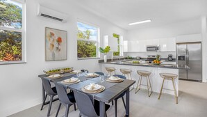 A modern kitchen with white cabinets, a stainless steel refrigerator, and a dining area with a table set for six. - UP TO 12 GUESTS! Modern house near Wynwood (Miami)