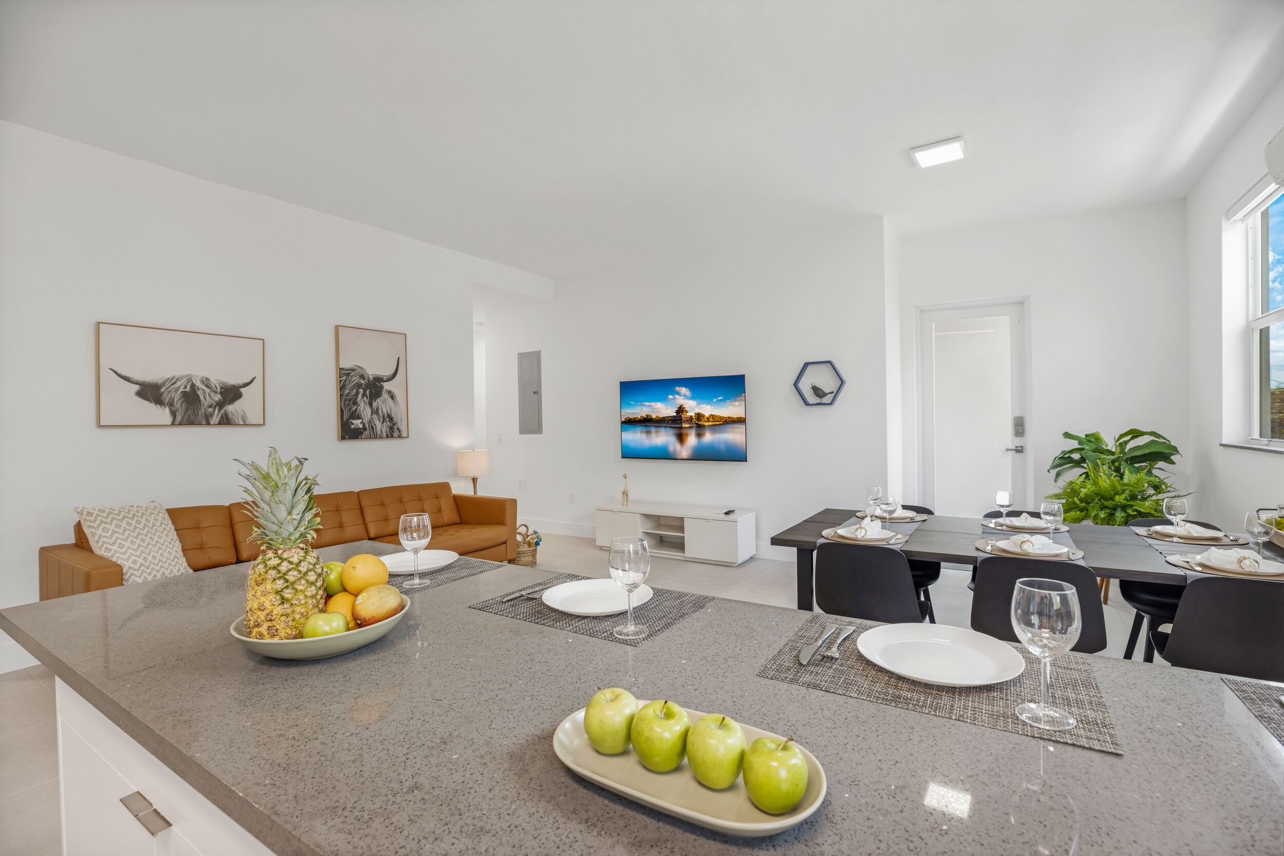 Una cocina moderna con encimera de granito, una zona de comedor con una mesa dispuesta para seis personas, y una sala de estar con sofá y una mesa de centro.