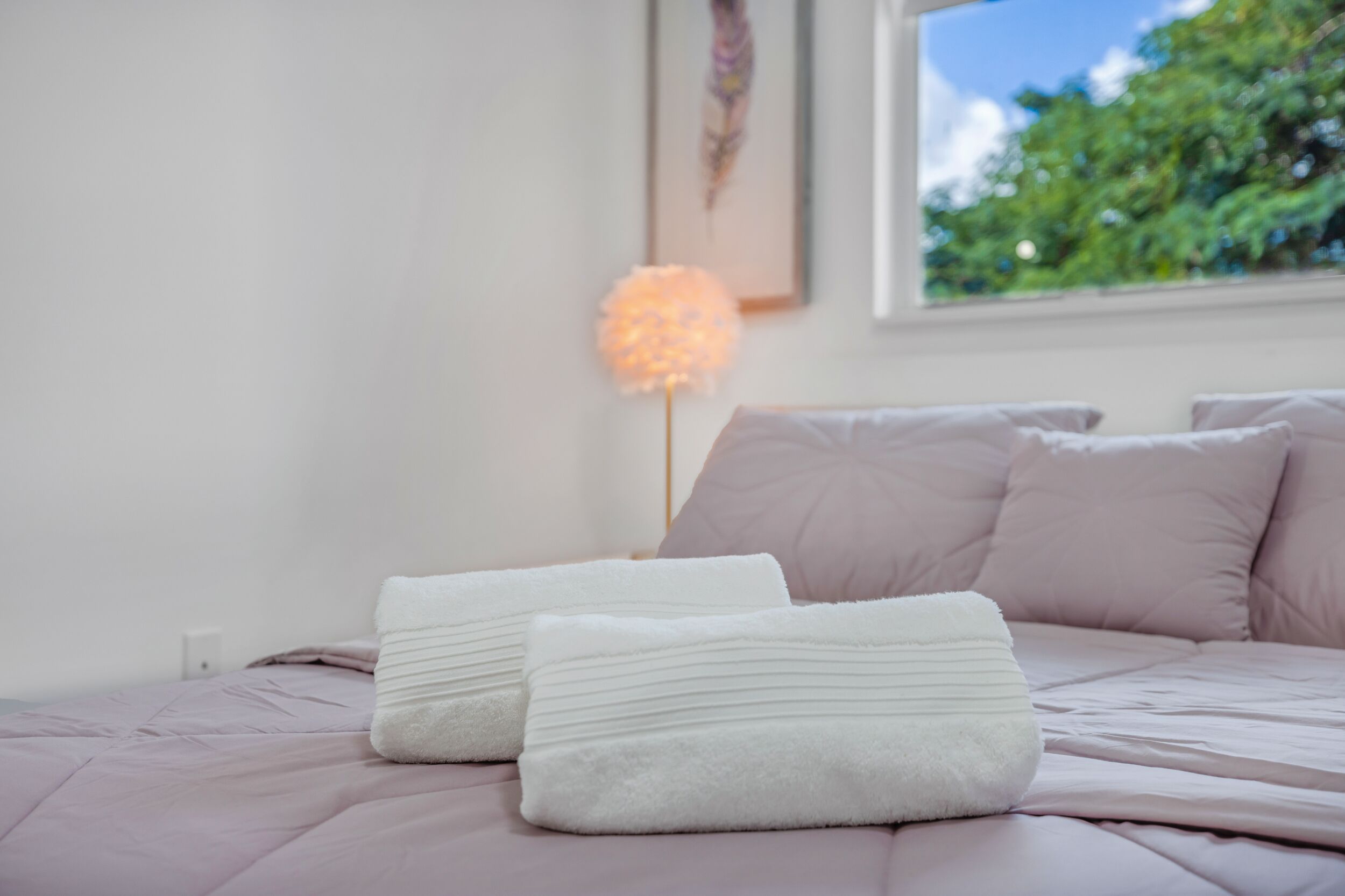 Een net opgemaakt bed met een roze dekbed en twee witte kussens.