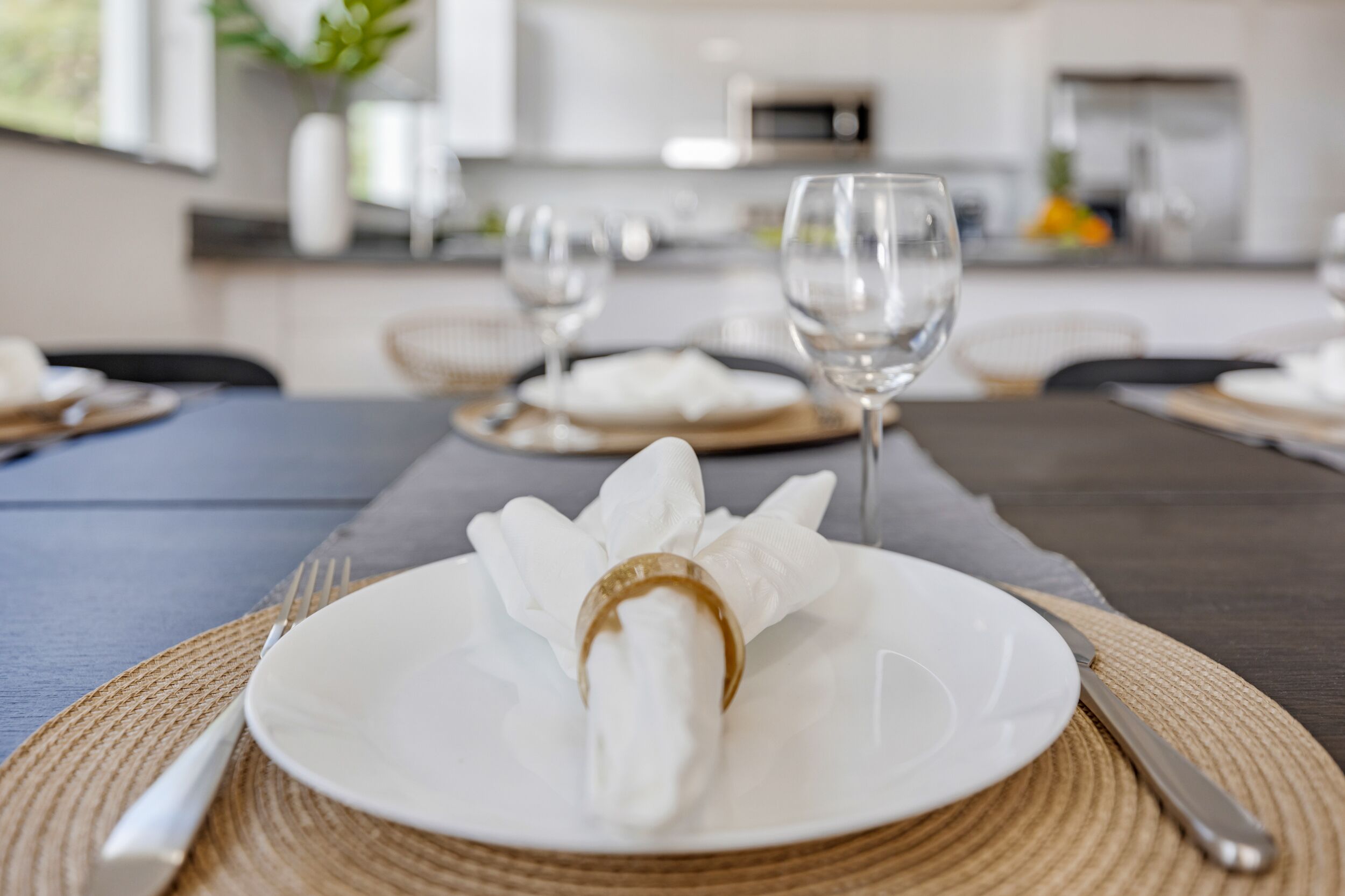Mesa de jantar posta com um prato branco, guardanapo e talheres, com um jogo americano tecido por baixo.