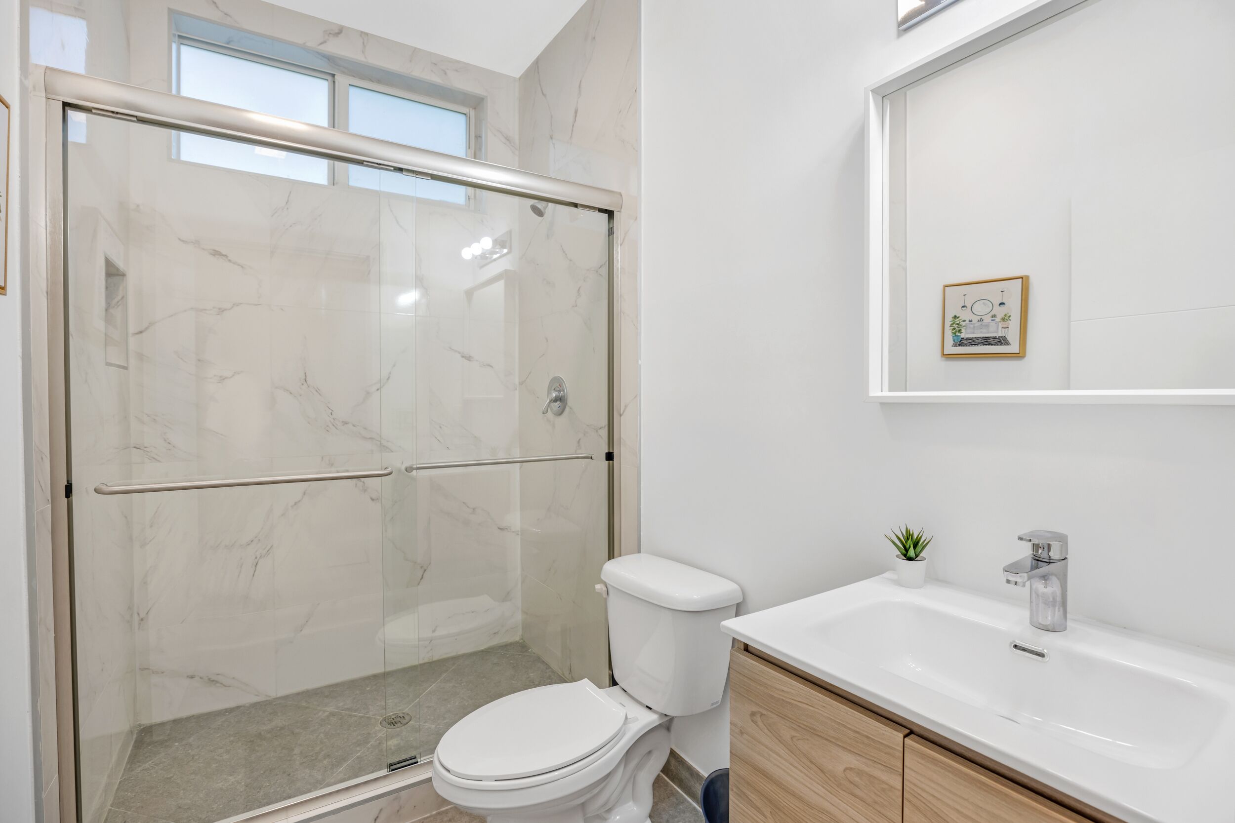A modern bathroom with a glass-enclosed shower, a white toilet, and a wooden vanity with a sink.