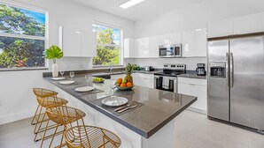 A modern kitchen with white cabinets, stainless steel appliances, a granite countertop, and a large window offering a view of greenery. - UP TO 12 GUESTS! Modern house near Wynwood (Miami)