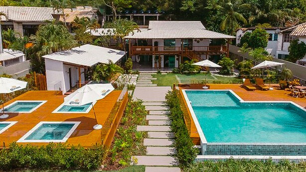 Ett semesterhotell med en swimmingpool, utomhusmöbler och en huvudbyggnad med en täckt innergård.