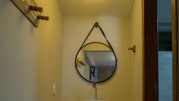 A bathroom with a round mirror, a white sink, and a ceiling light fixture.