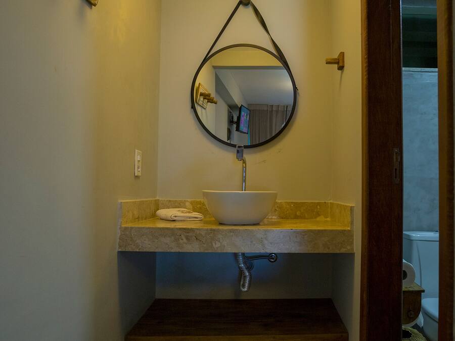 A bathroom with a round mirror, a white sink, and a ceiling light fixture.
