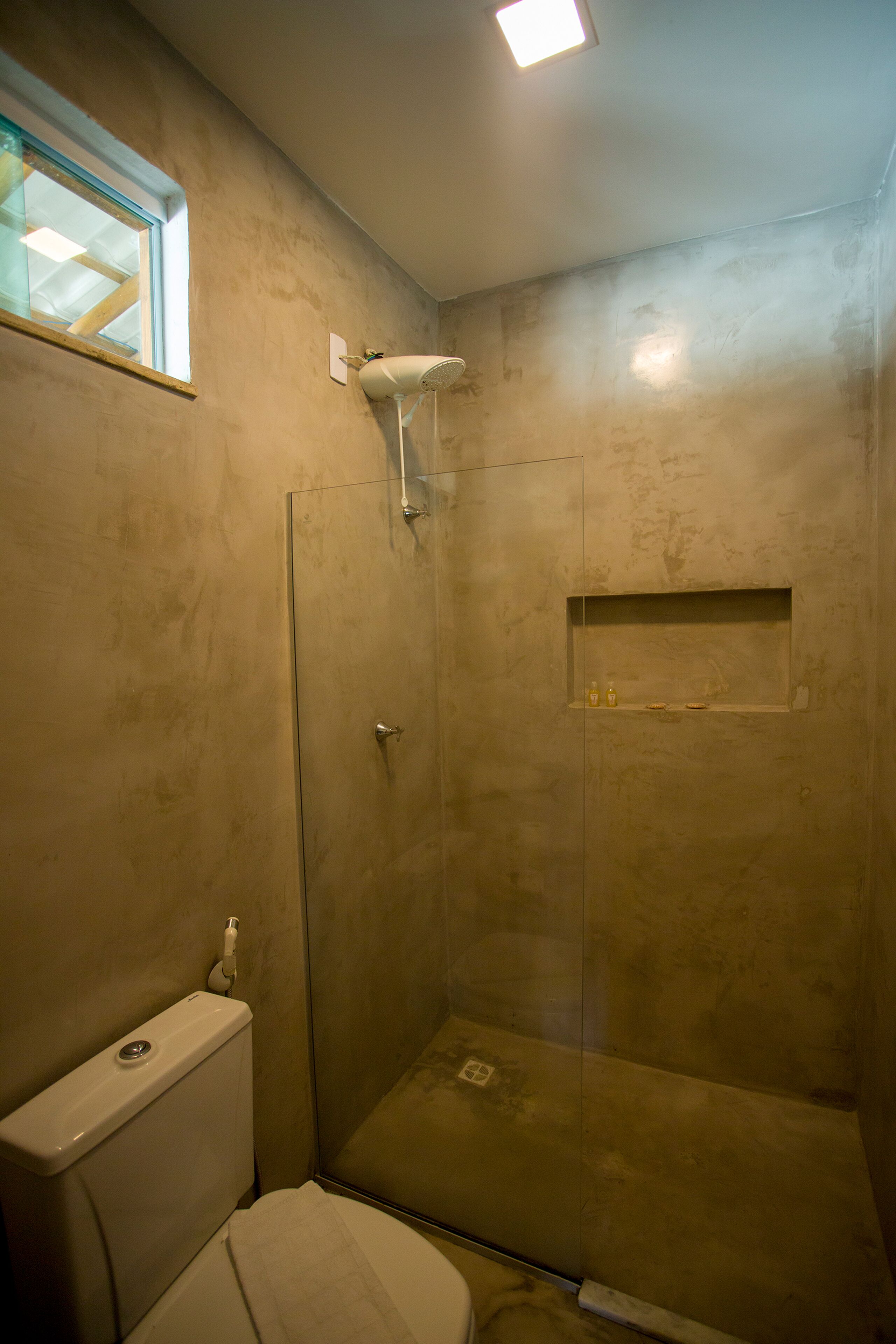 Un petit espace douche fermé, doté d’une porte en verre, de toilettes et d’une étagère contenant des articles de toilette.